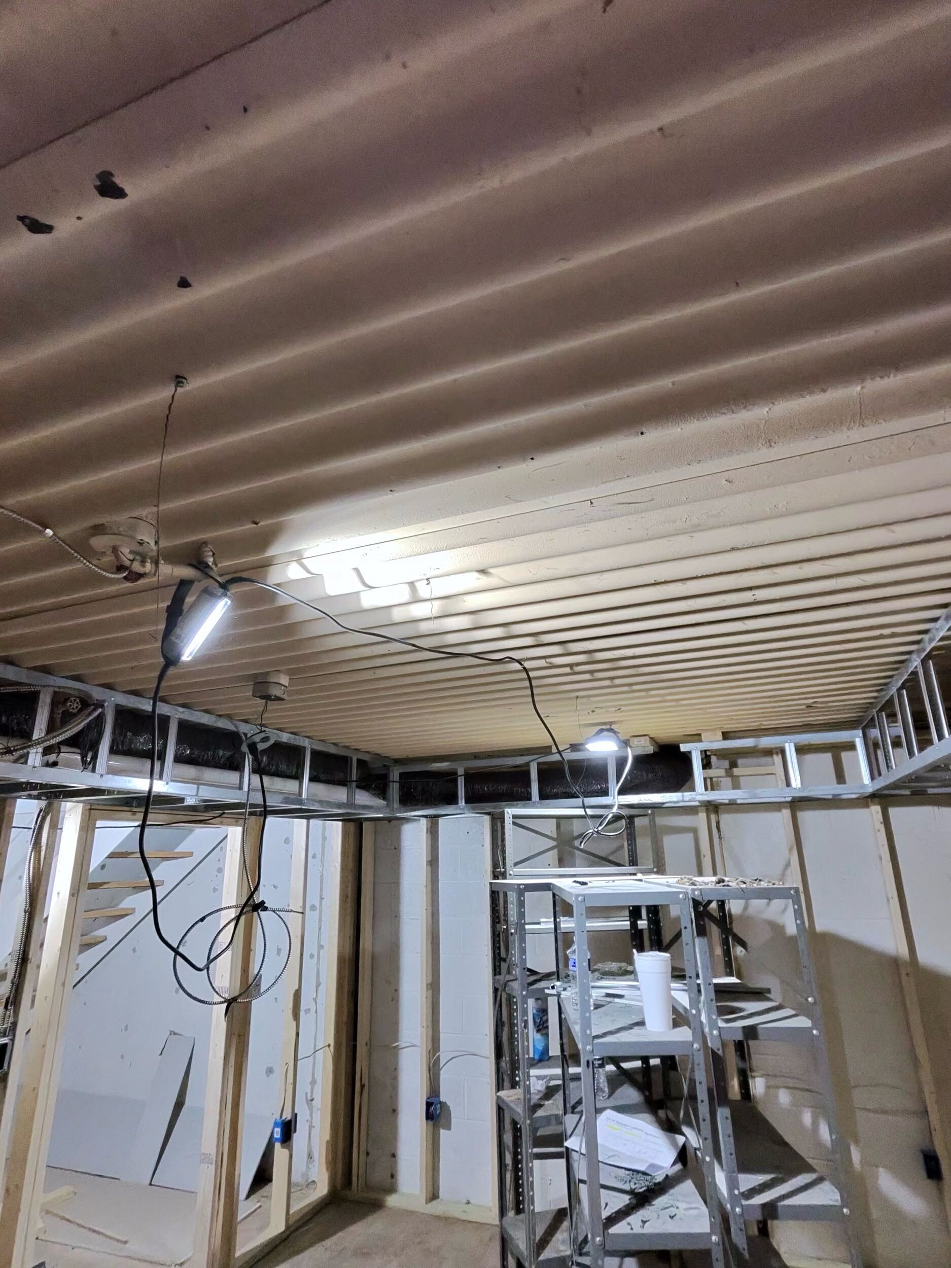 Basement ceiling with exposed metal deck, temporary lighting, wiring, and open wall framing